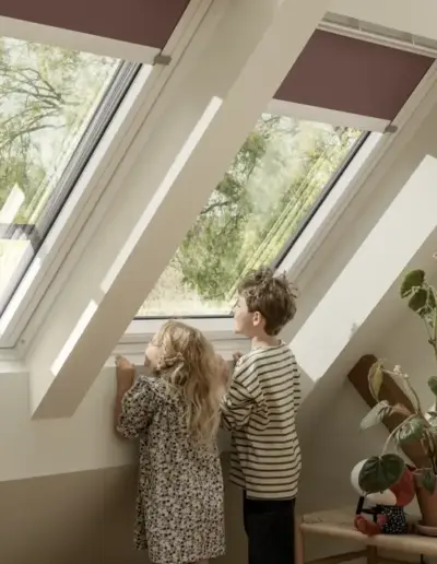 Zwei Kinder blicken durch eine Fensterkombination im Dachgeschoss nach draußen.