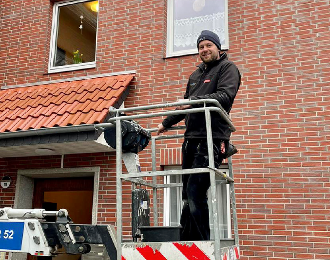 Marcel Saß auf einer Hebebühne vor einem Backsteinhaus.
