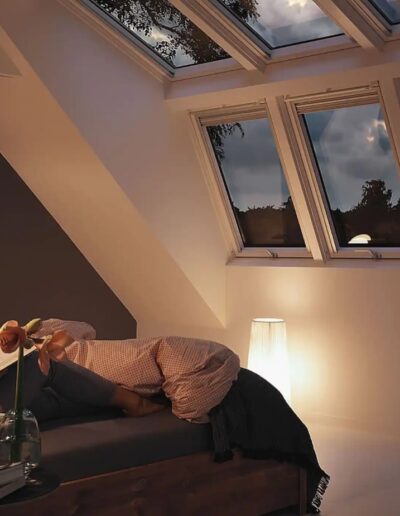 Schlafzimmer unter dem Dach mit großer Fensterkombination in der Abenddämmerung.