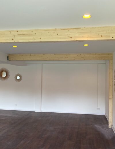 Innenraum mit sichtbaren Holzbalken und eingelassenen Deckenleuchten.