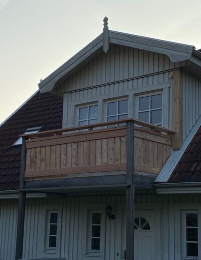Holzbalkon vor einem hell verkleideten Dachgiebel.
