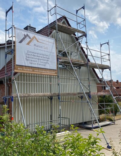 Eingerüstete Giebelfassade mit senkrechter Verkleidung und Firmenbanner.