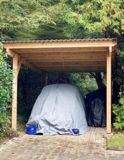 Carport aus Holz mit einem abgedeckten Fahrzeug.