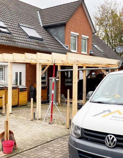 Holzkonstruktion einer Überdachung vor einem Klinkerhaus mit Firmenfahrzeug.