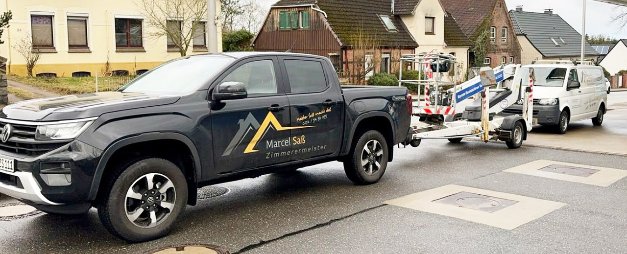 Firmenfahrzeuge mit Anhänger und Baumaterial auf einer Straße.