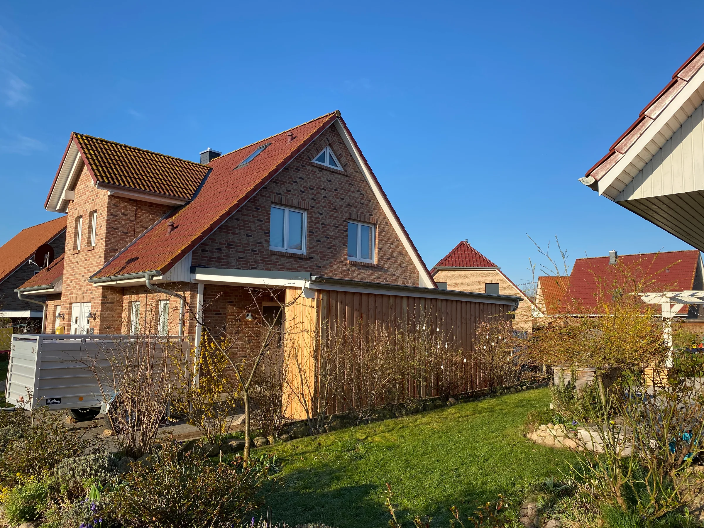 Klinkerhaus mit seitlichem Holzanbau und Garten.